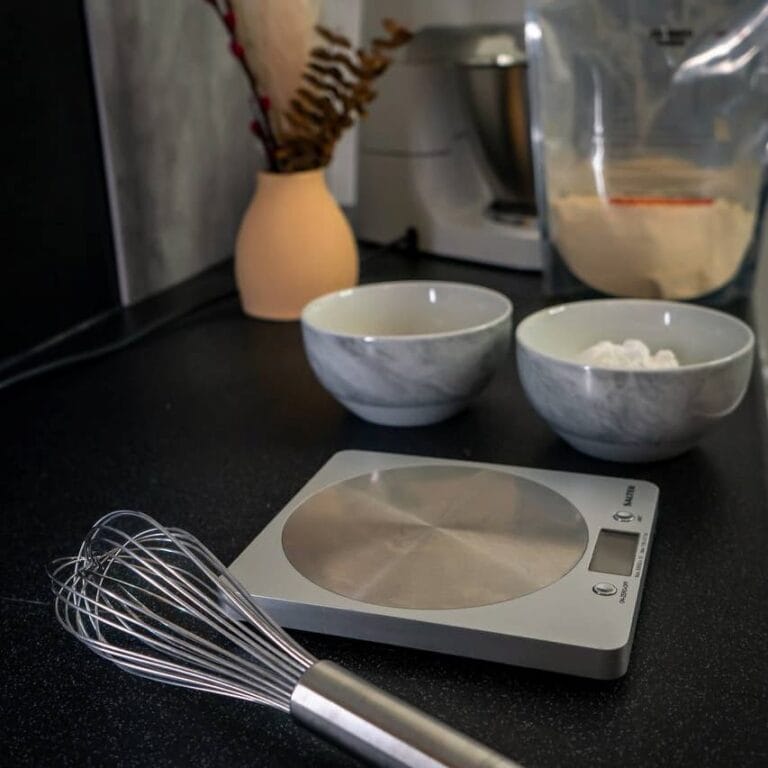 Baking tools and ingredients on a kitchen counter, including a whisk, digital scale, and bowls with flour and sugar