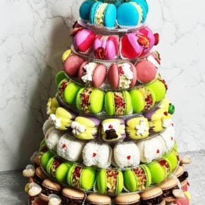 The 10-tier Macaron Tower displays a pyramid of colorful macarons and small desserts in vibrant pink, green, brown, and blue hues, enhanced by white cream-filled treats and decorative flowers.