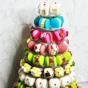 An 8-tier macaron tower boasts a dazzling array of colorful macarons and petite pastries. Each layer presents different hues—blue, pink, green, and white—artfully arranged against a marble-patterned background.