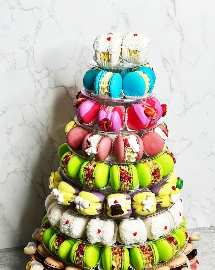 An 8-tier macaron tower boasts a dazzling array of colorful macarons and petite pastries. Each layer presents different hues—blue, pink, green, and white—artfully arranged against a marble-patterned background.