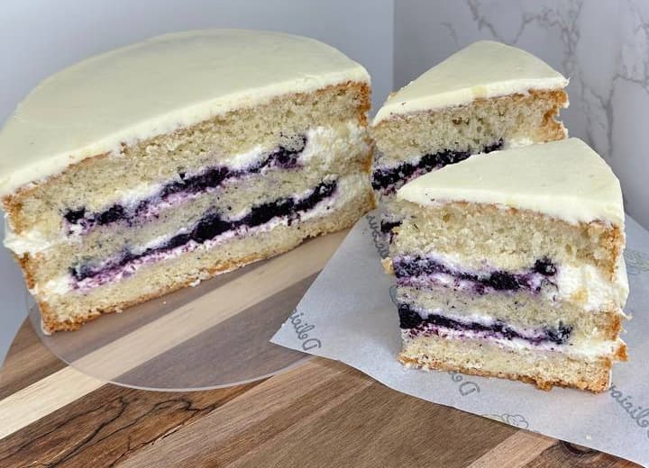 A round layer cake with white icing, two slices cut out, and visible layers of cream and dark berry filling inside.